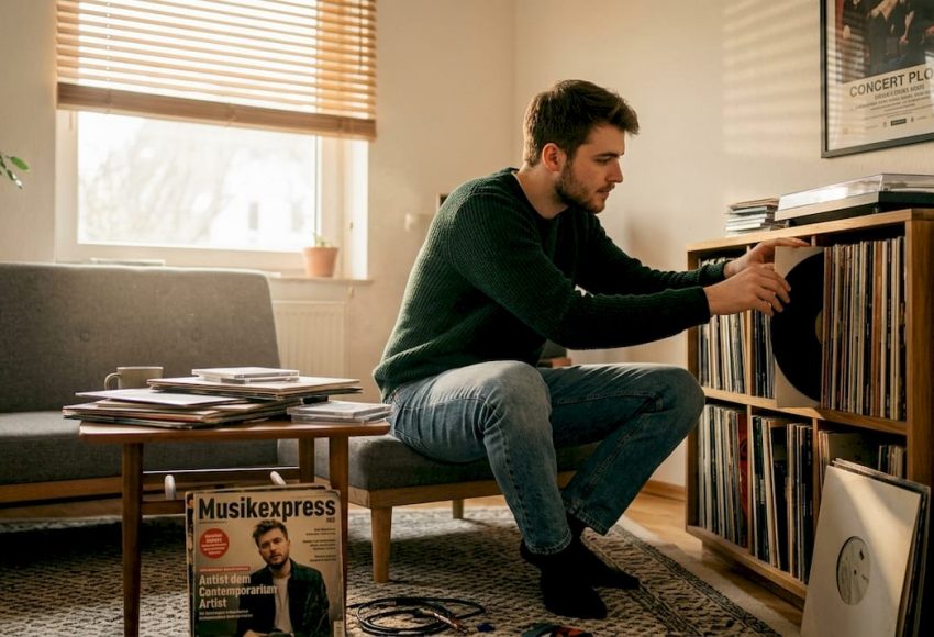 Musikgenres einfach erklärt: Überblick für Events 9 Im Wohnzimmer sortiert eine Person Schallplatten an einem Holzregal, warmes Tageslicht fällt durch das Fenster und unterstützt das Thema Musikgenres für Events.
