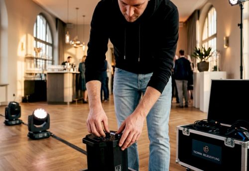 Lichttechnik für Feiern erklärt: Profi-Tipps für München 4 Ein Techniker richtet Lichttechnik für Feiern ein und steuert Effekte im DMX-System in einer Indoor-Halle in München, mit schwarzer Hardware.