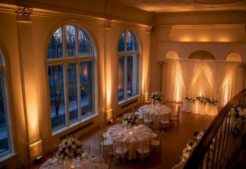 Ambientebeleuchtung Hochzeit: Stimmungsvoll planen und buchen 3 Warmweißes Licht erhellt einen festlich gedeckten Hochzeitssaal mit hohen Fenstern und sanft angestrahlten Wänden.
