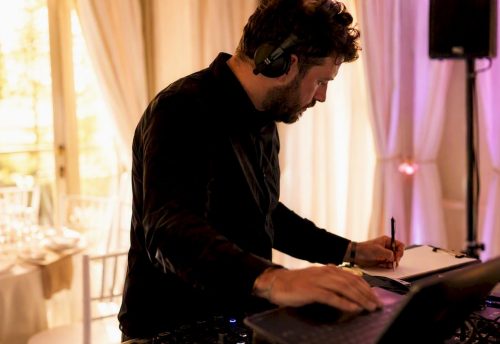 No-Go-Lieder auf der Hochzeit: Was Paare besser vermeiden 5 Ein Hochzeits-DJ mit Kopfhörern notiert Songs am Mischpult und steuert den Laptop bei einer Feierlocation.