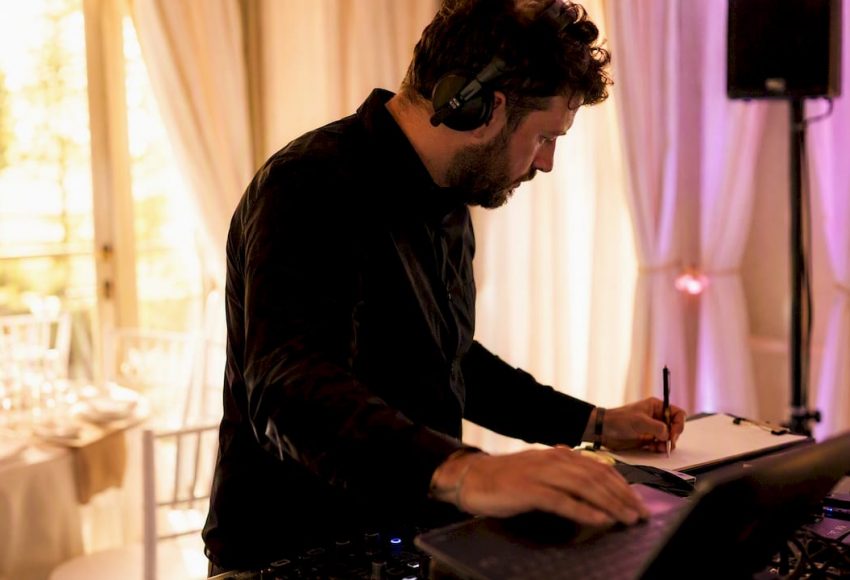 No-Go-Lieder auf der Hochzeit: Was Paare besser vermeiden 1 Ein Hochzeits-DJ mit Kopfhörern notiert Songs am Mischpult und steuert den Laptop bei einer Feierlocation.