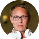 Ein DJ mit Brille und Kopfhörern, der in die Kamera schaut.